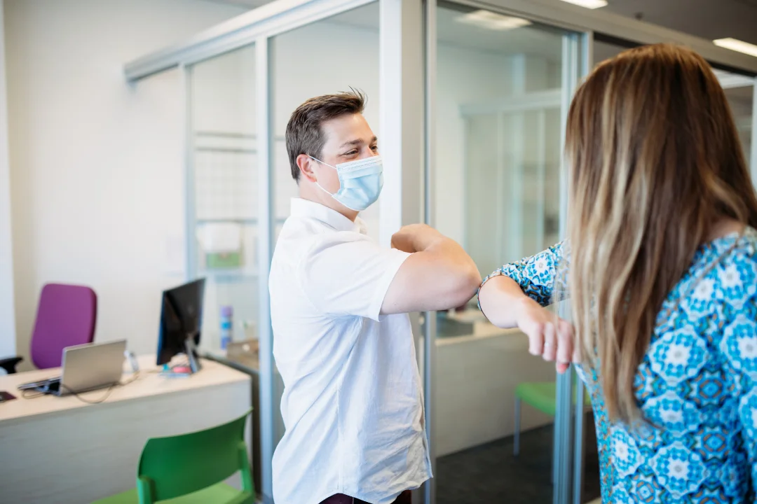 Office employees returning to work after covid wearing masks and elbow bumping instead of shaking hands