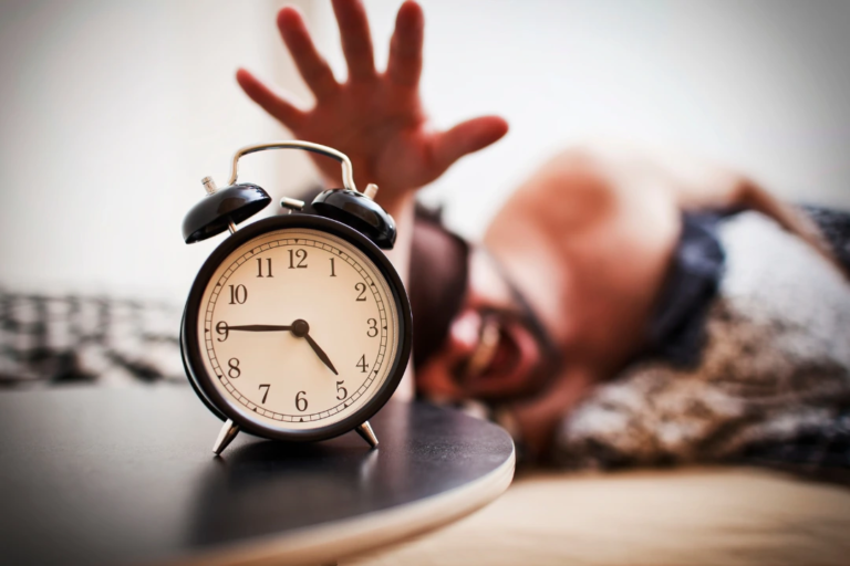 Close-up of alarm clock at 5:45 AM with person in bed, symbolizing how early routines can contribute to being a better HR leader.