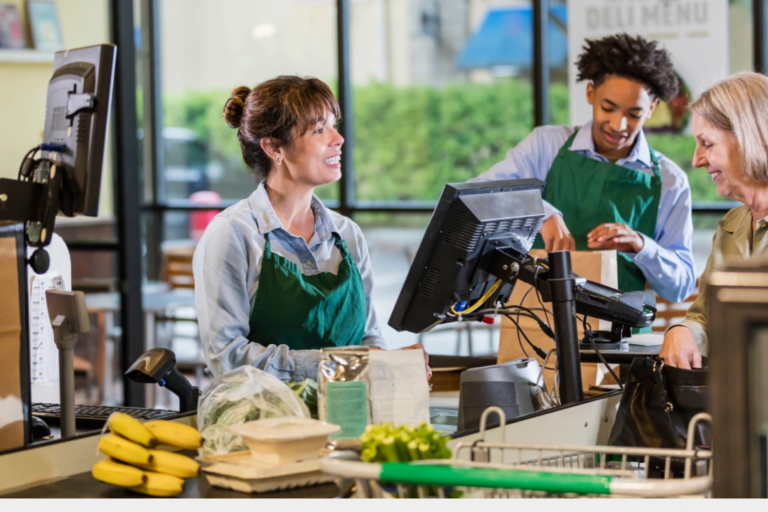 Two hourly employees in aprons helping a smiling customer, representing an example of the positive workplace culture hourly workers want to be part of.